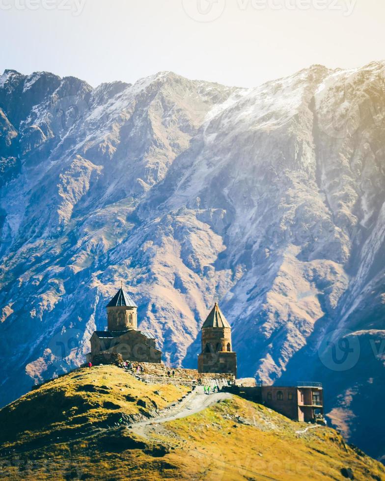 Stepantsminda, Gergeti, Georgia. Famous Gergeti Trinity Tsminda Sameba Church In Early Winter Landscape. Suv Moving Near Church In Beautiful Georgian Landscape In Early Winter photo