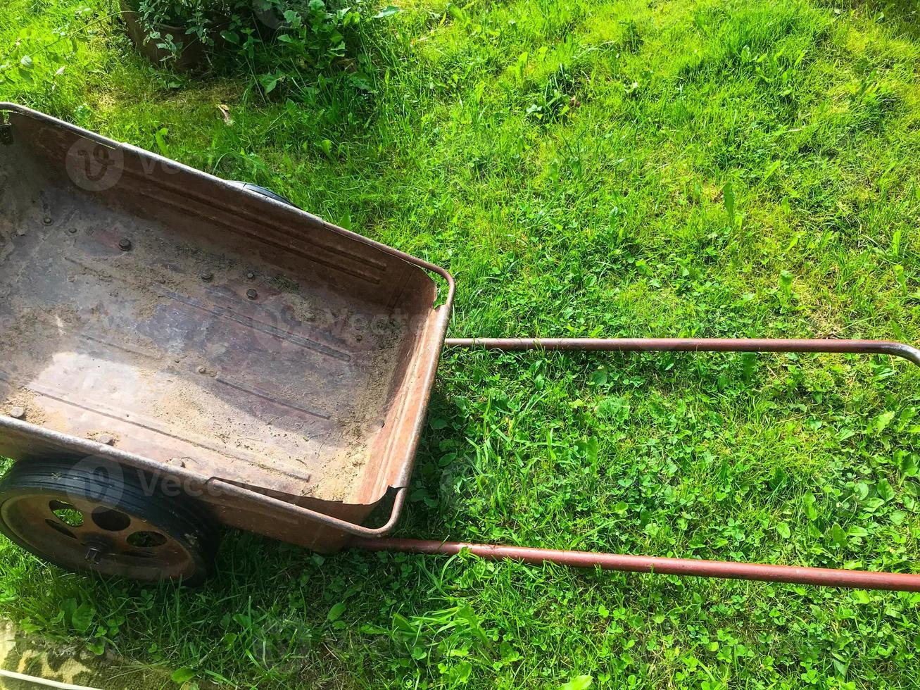 a metal wheelbarrow for transporting products and fertilizers stands on the green grass. a wheelbarrow for garden work. gardener, gardener inventory. garden care photo