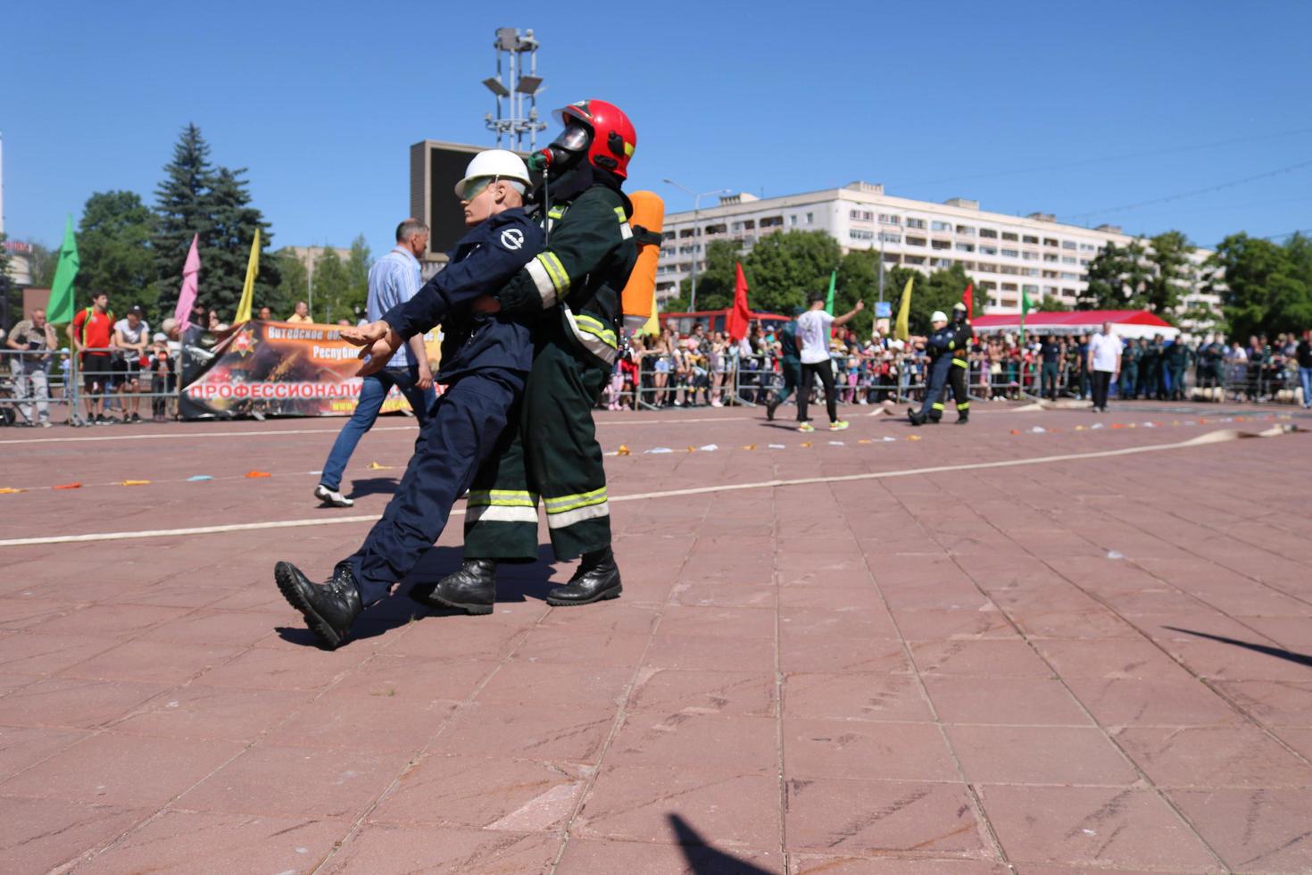 Men firefighter in fireproof suit and helmet rescues drags pulls maniken of worker's man out of danger at exercises, at fire-fighting competitions, Minsk, Belarus, 06.06.2018 photo