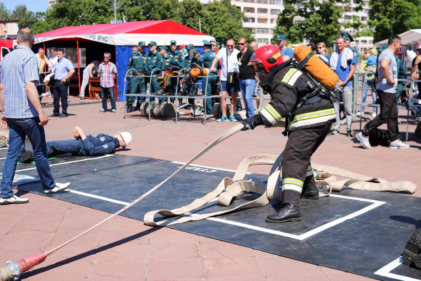 A fireman in a fireproof suit and a helmet running with an oxygen balloon pulling, holding a fire hose at a fire sport competition. Minsk, Belarus, 08.07.2018 photo