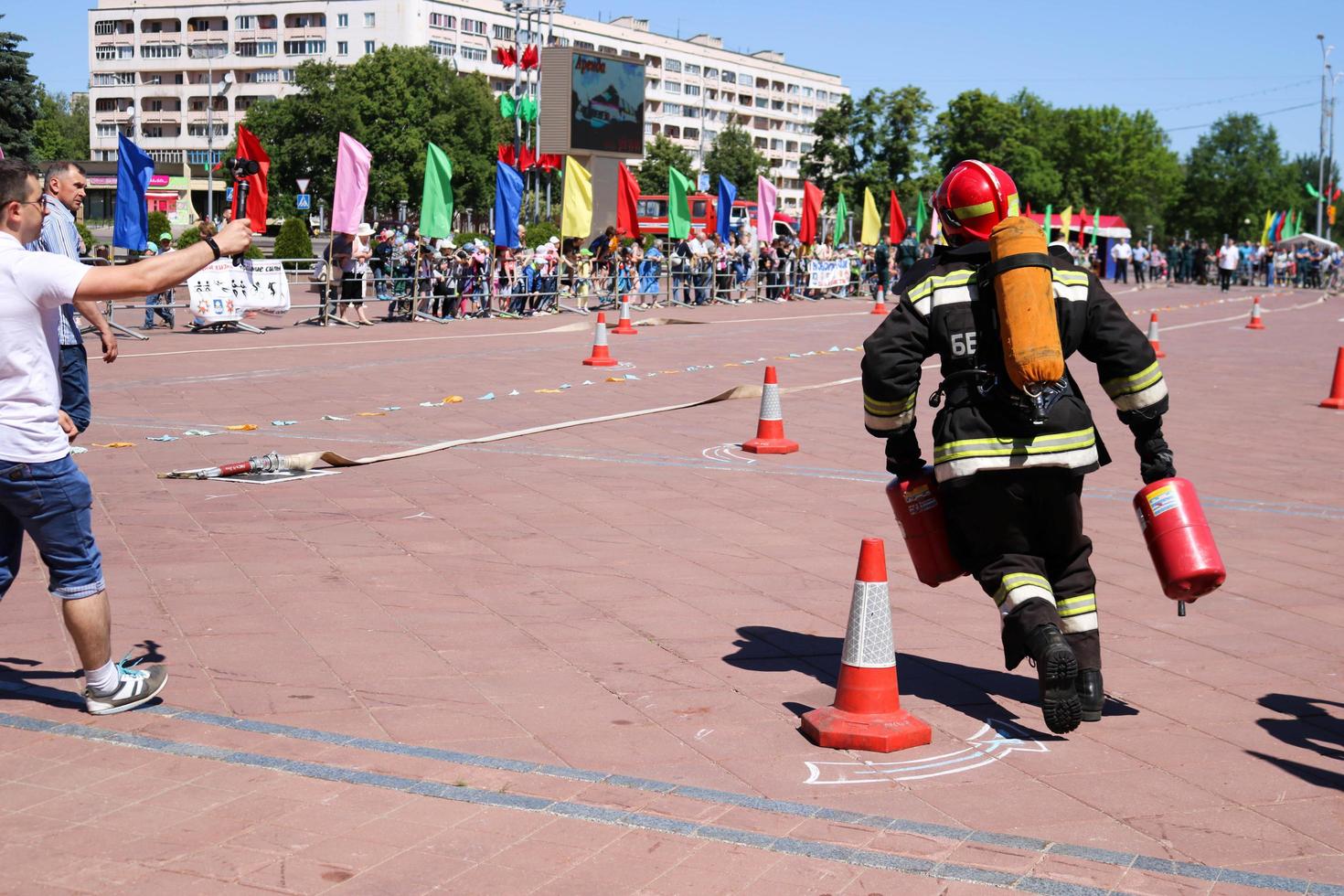 A fireman in a fireproof suit and a helmet running with red fire extinguishers to extinguish a fire at a fire sport competition, Belarus, Minsk, 08.08.2018 photo