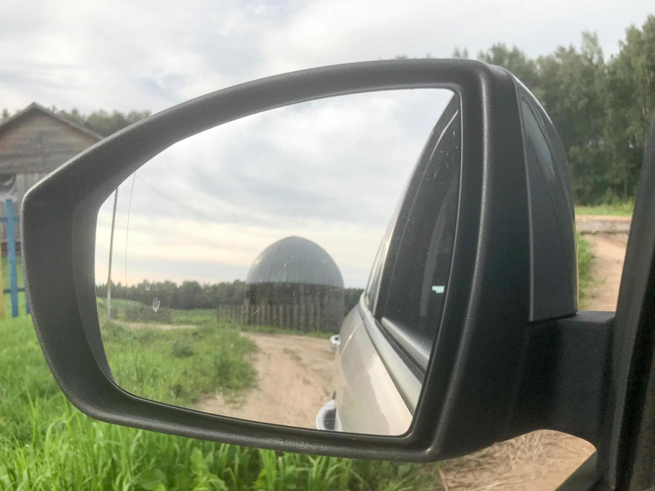 A large round concrete and metal barn for storing grain and corn in the car's rear-view mirror photo