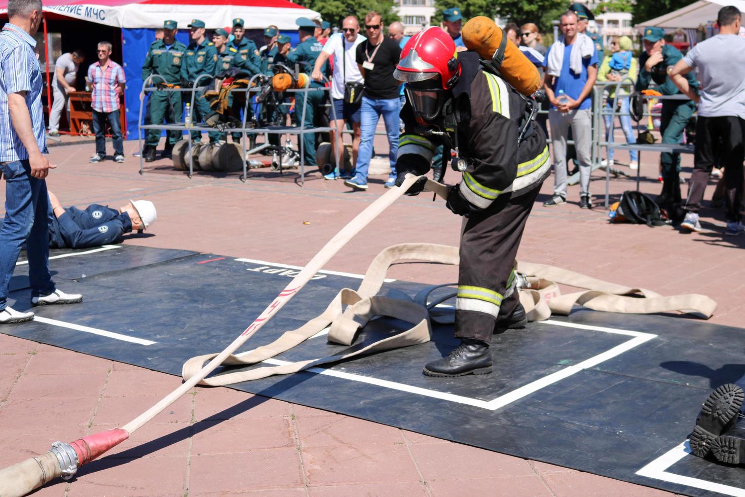 A fireman in a fireproof suit and a helmet running with an oxygen balloon pulling, holding a fire hose at a fire sport competition. Minsk, Belarus, 08.07.2018 photo