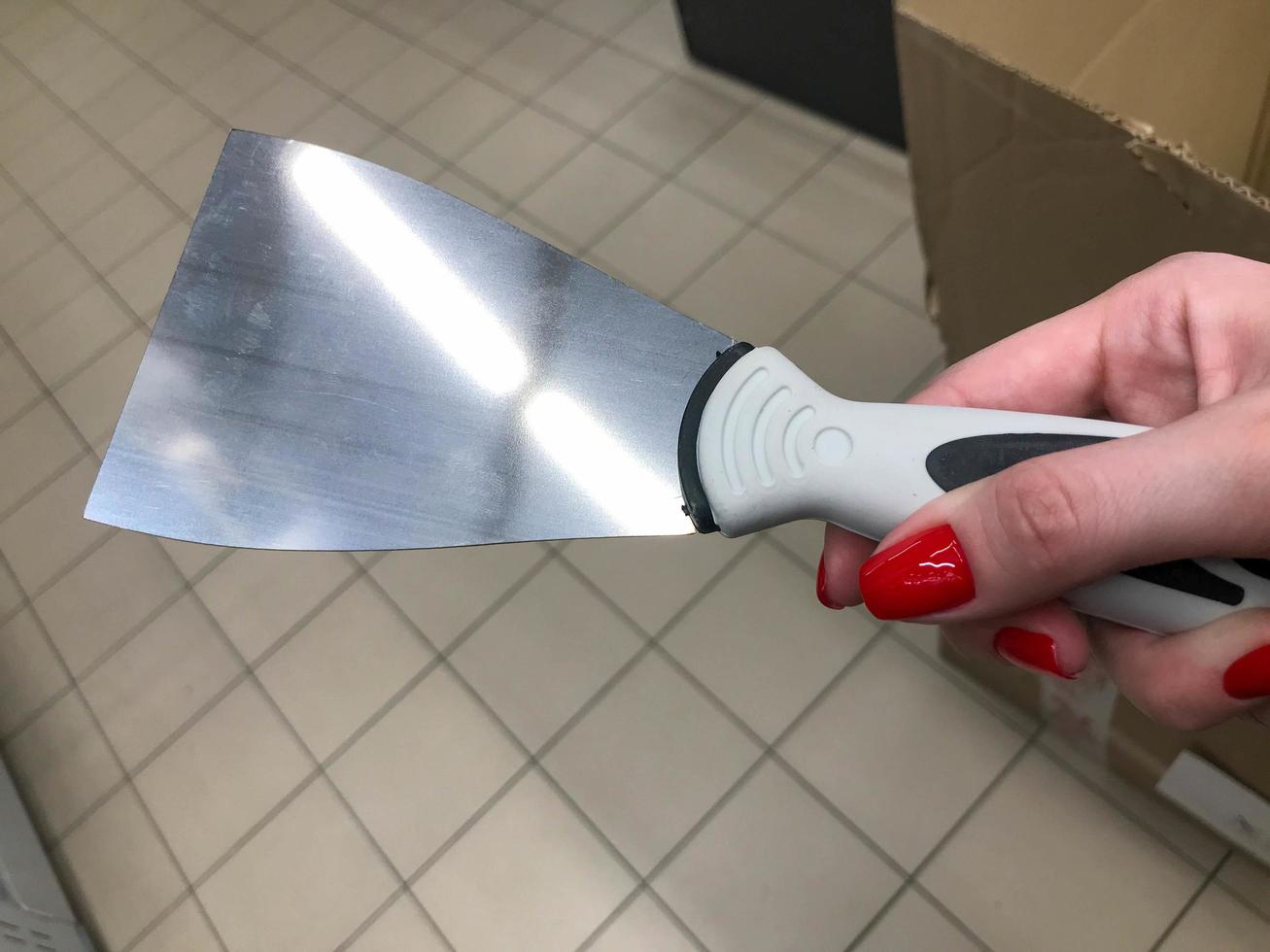 raspador para aplicar masilla, yeso. trabajos de pintura. reparación casera de bricolaje. un raspador en manos de una mujer con una manicura roja brillante. trabajo de reparación realizado por una mujer foto