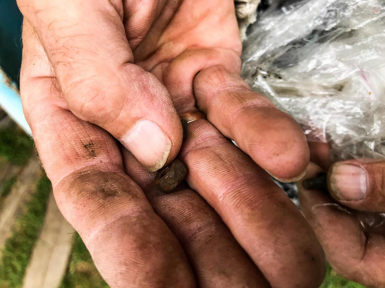 el hombre tiene varias herramientas de reparación en sus manos. un hombre atraviesa clavos, tuercas, pernos. en la mano hay pequeñas herramientas para el trabajo. manos sucias manchadas con aceite combustible negro foto