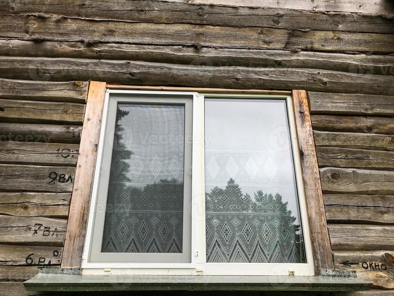 the window is wooden in the frame. wooden house in the village. glass window with painted wooden frame. there is a curtain hanging on the window, tulle made of white thin material photo