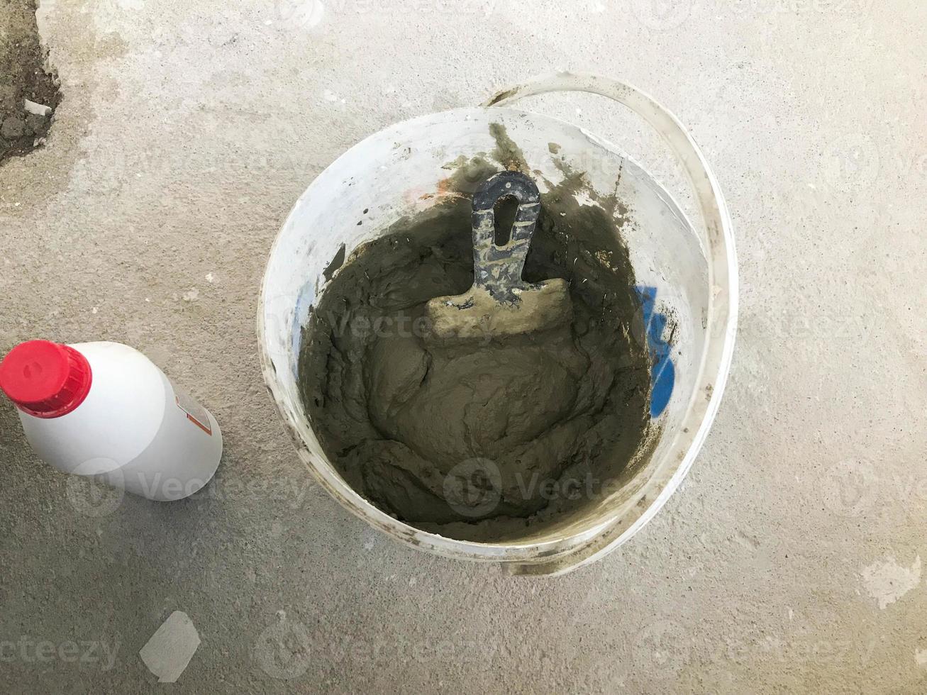 Large white plastic construction bucket with spatula and plaster, tiled glue, cement for the repair of an apartment, house, leveling the walls and pouring screed on the floor photo