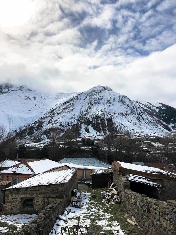 Small stone houses, buildings in the village on a beautiful mountain cold winter resort with high mountain peaks mist and snow covered rocks for snowboarding and skiing against a blue sky photo