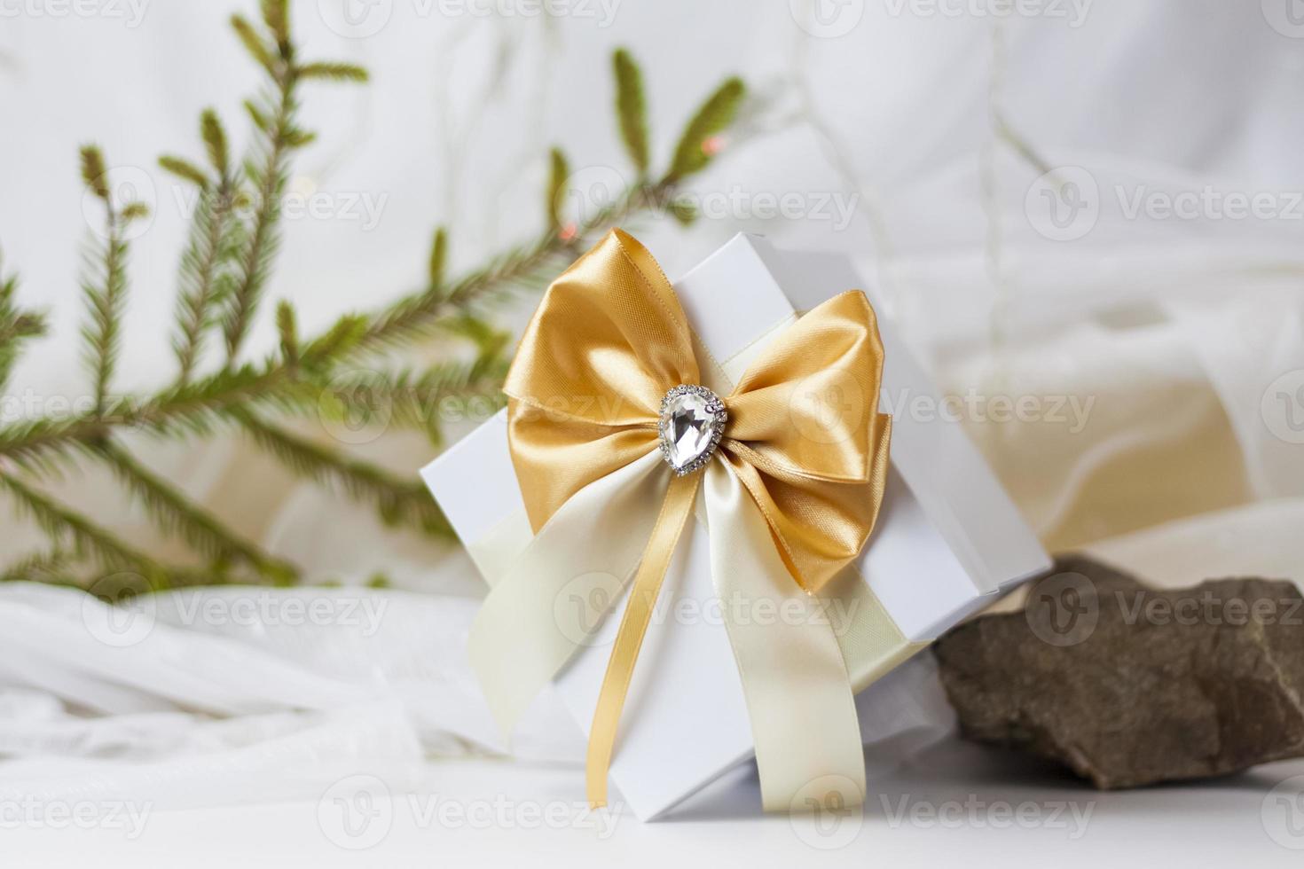 A Christmas gift decorated with a beautiful bow on a light background with a twig, if. Selective focus. the concept of Christmas and New Year. photo