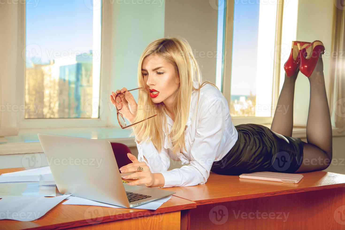Secretaria de oficina rubia sexual en camisa posando sobre la mesa foto
