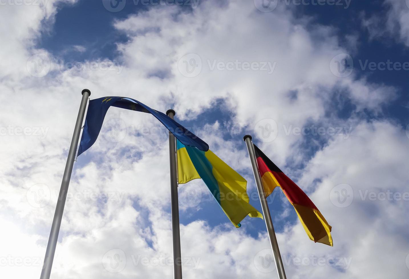 Flags of Ukraine, Germany and European Union fly side by side against blue sky. photo