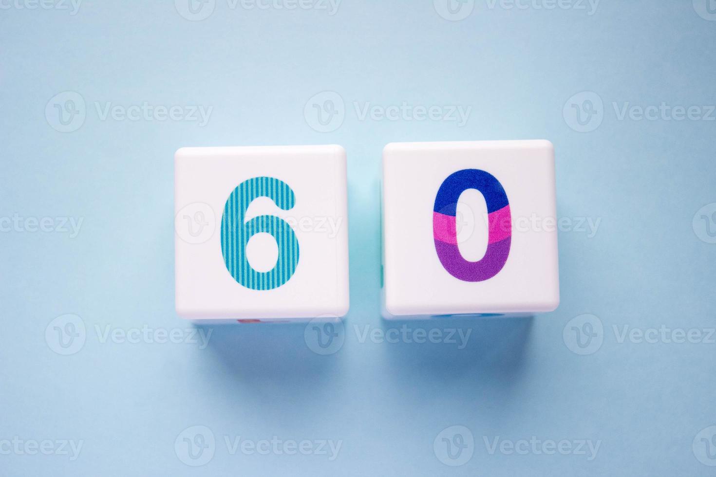 Close-up photo of a white plastic cubes with a colorful number 60 on a blue background. Object in the center of the photo