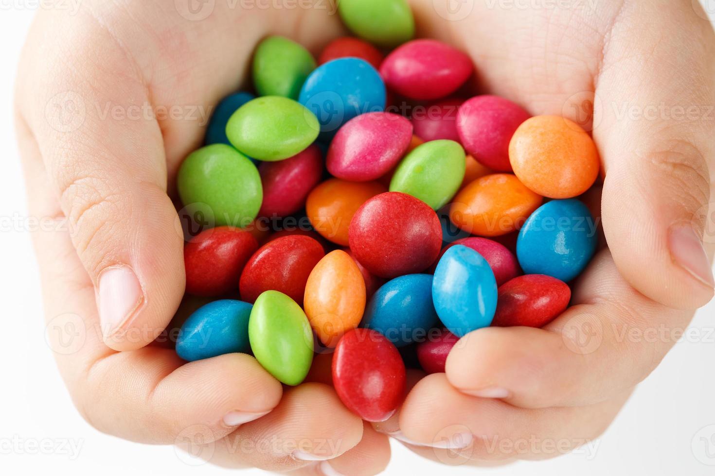 Multicolored candies in the hands of a child on a white isolated background photo