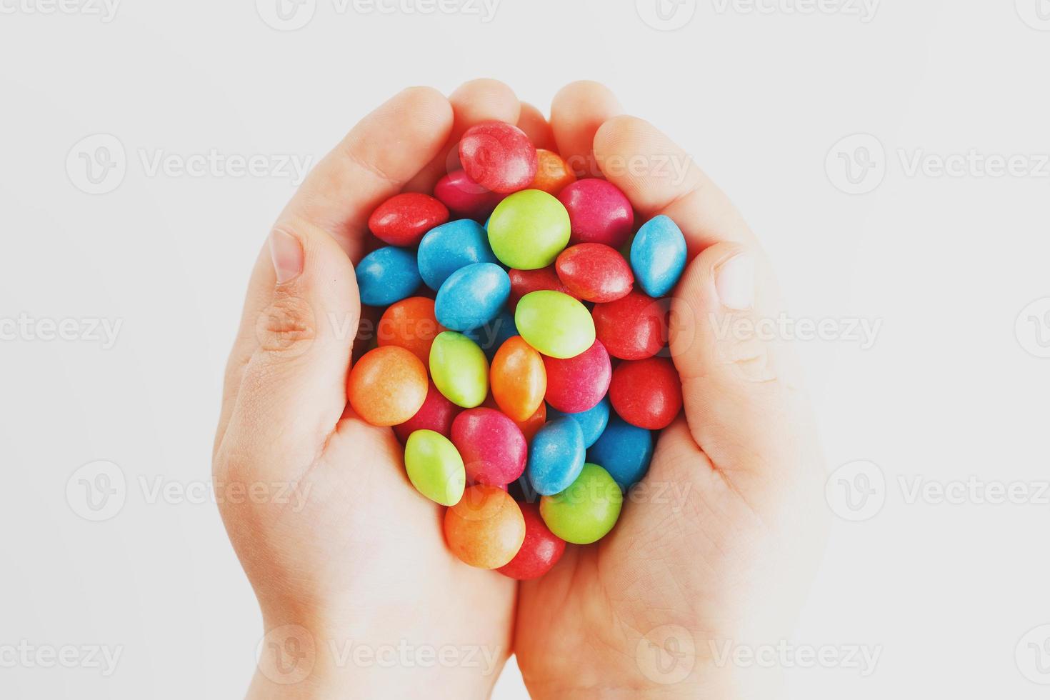 caramelos multicolores en manos de un niño sobre un fondo blanco aislado. bajo contraste foto