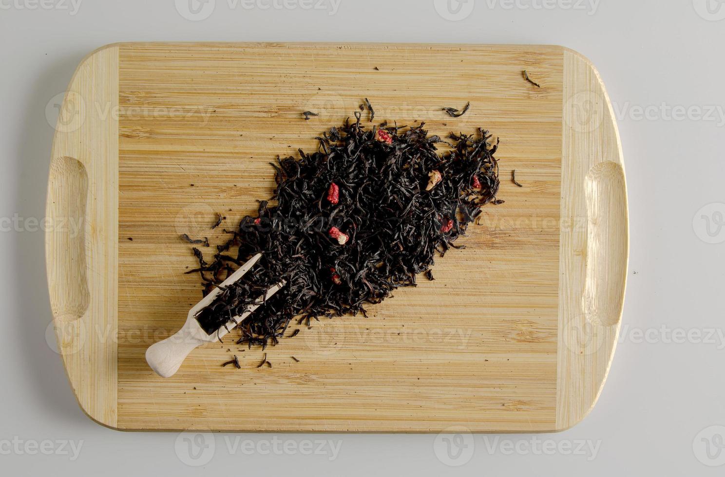 A mixture of dry black tea and pieces of dried strawberries as a background. Isolated on a wooden surface. photo