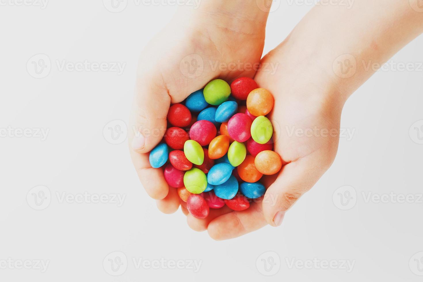 Multicolored candies in the hands of a child on a white isolated background. Low contrast photo