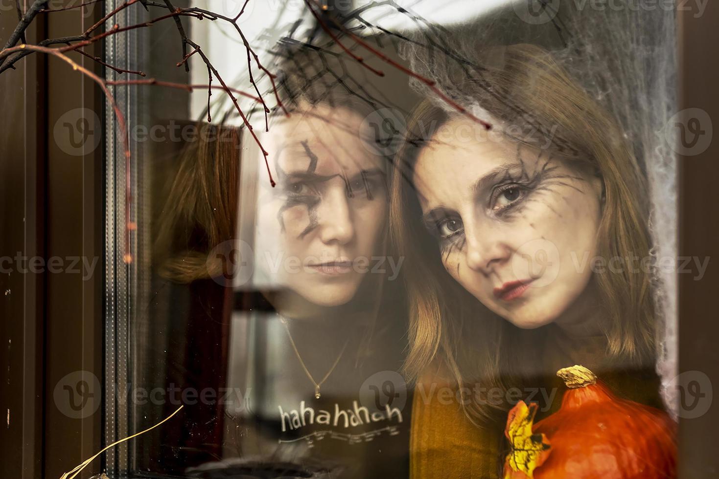 Two female witches look through a spider web ominously out of the window against the backdrop of Halloween decorations. Masquerade, Halloween party photo