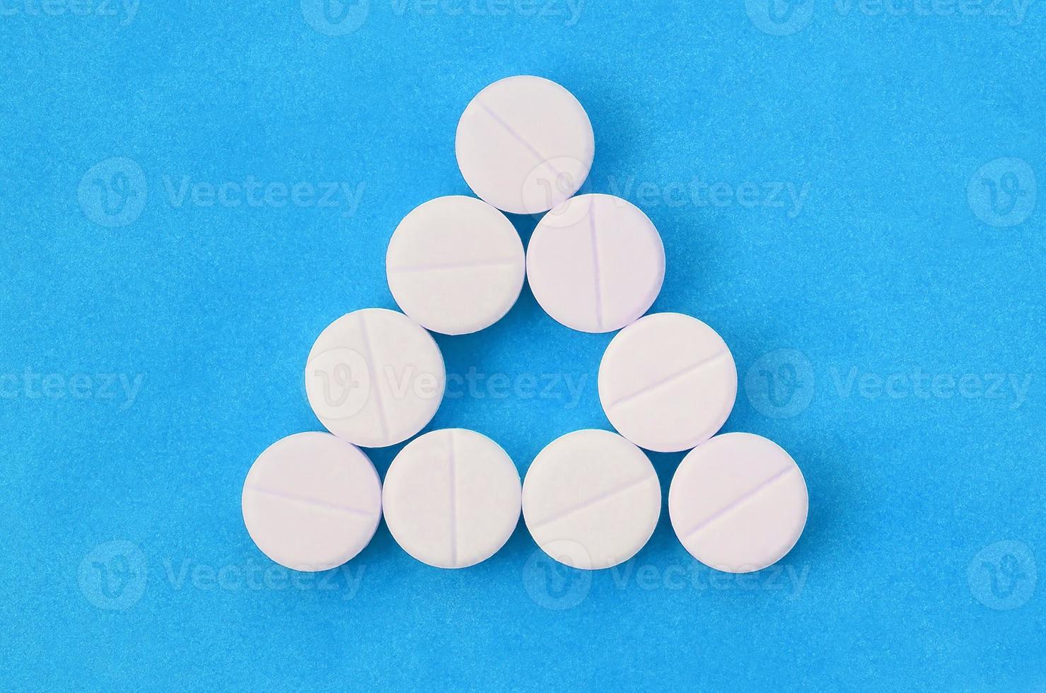 Several white tablets lie on a bright blue background in the form of an even triangle. Background image on medicine and pharmaceutical topics photo