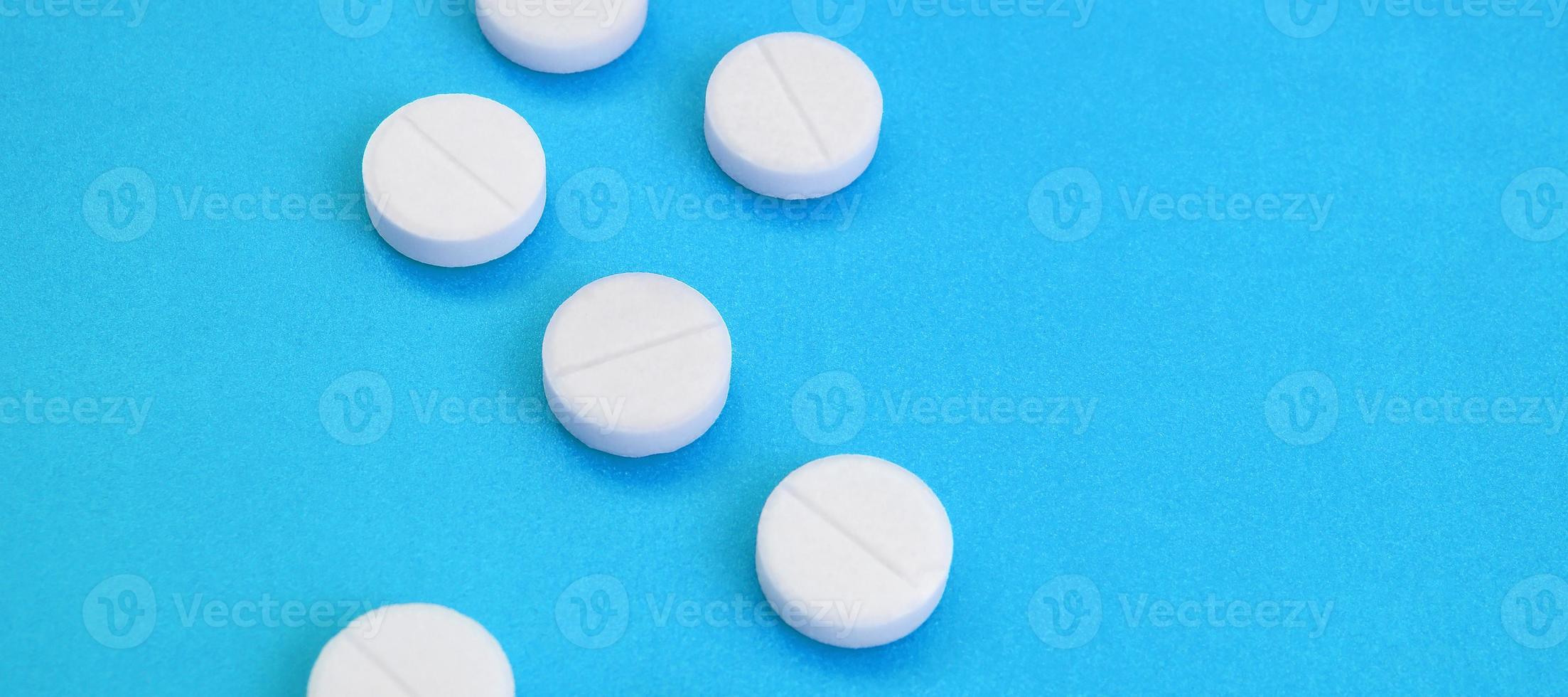 A few white tablets lie on a bright blue background surface. Background image on medical and pharmaceutical topics photo