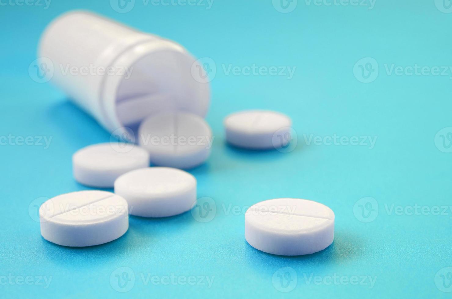 Several white tablets fall out of the plastic jar on the blue surface. Background image on medical and pharmaceutical topics photo