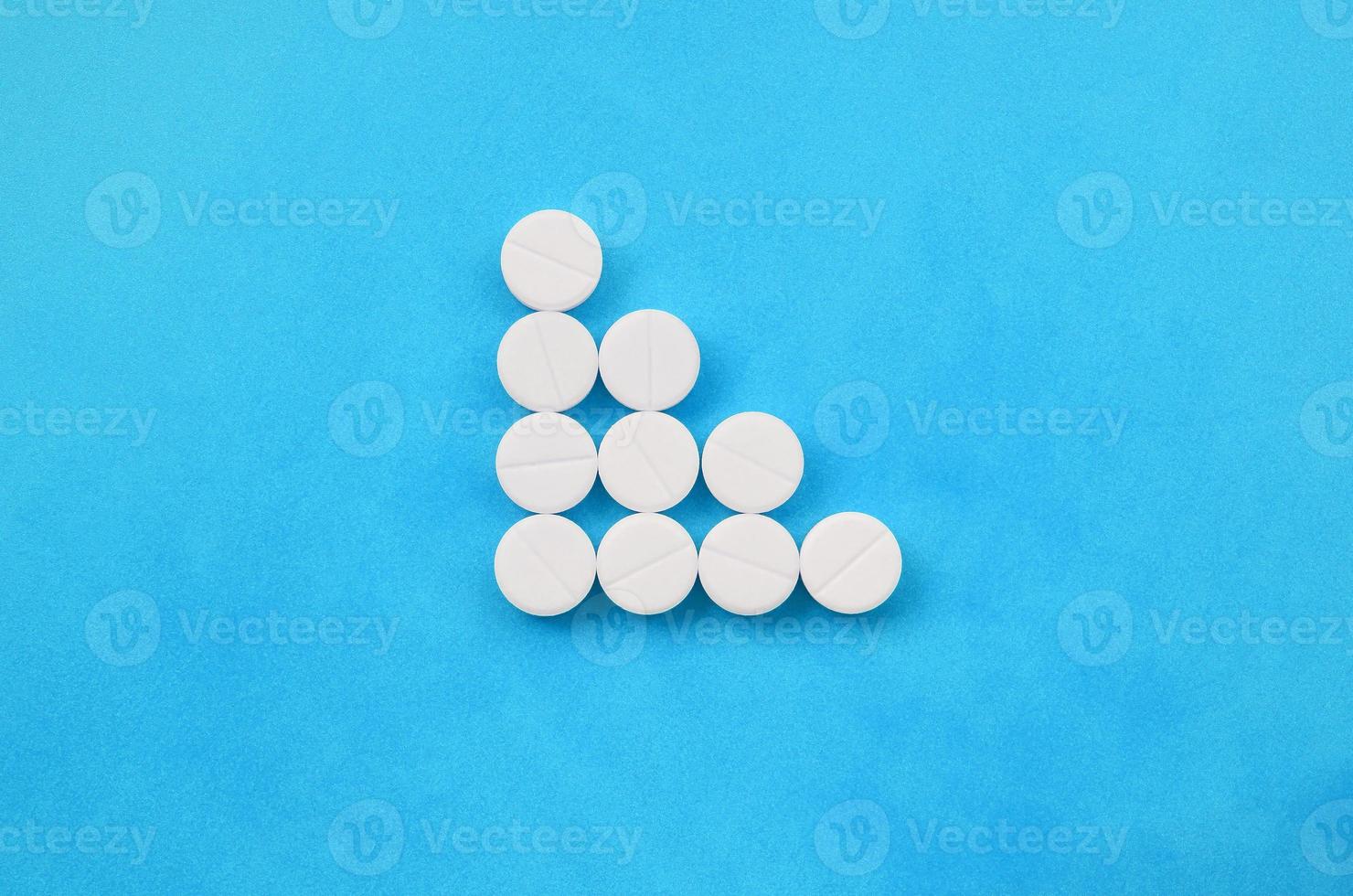 Several white tablets lie on a bright blue background in the form of a triangular arrow. Background image on medicine and pharmaceutical topics photo