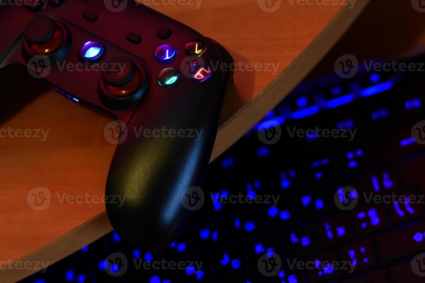 Modern gamepad lies with pc keyboard on table in dark playroom scene. Lets play video games together with friends concept photo