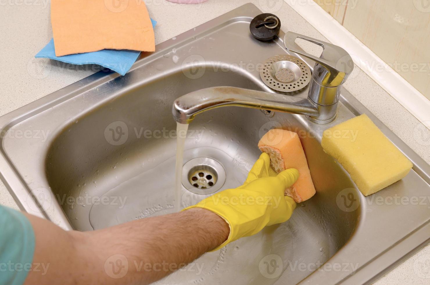 persona o amo de casa limpiando el fregadero de la cocina con una esponja a la vista foto