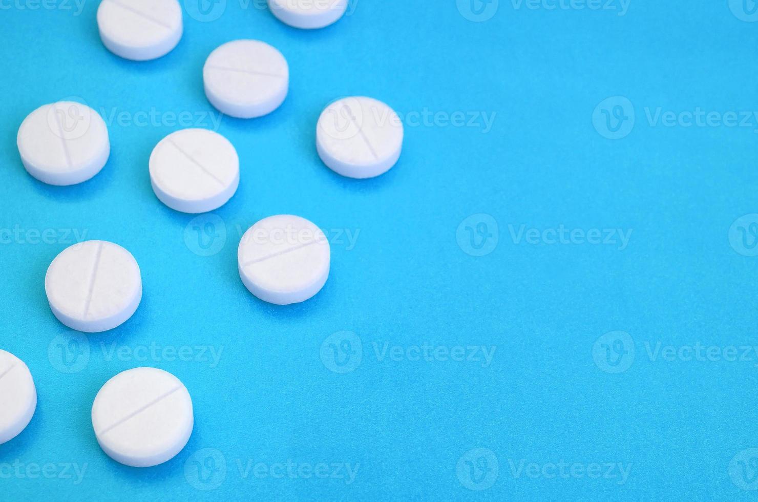 A few white tablets lie on a bright blue background surface. Background image on medical and pharmaceutical topics photo