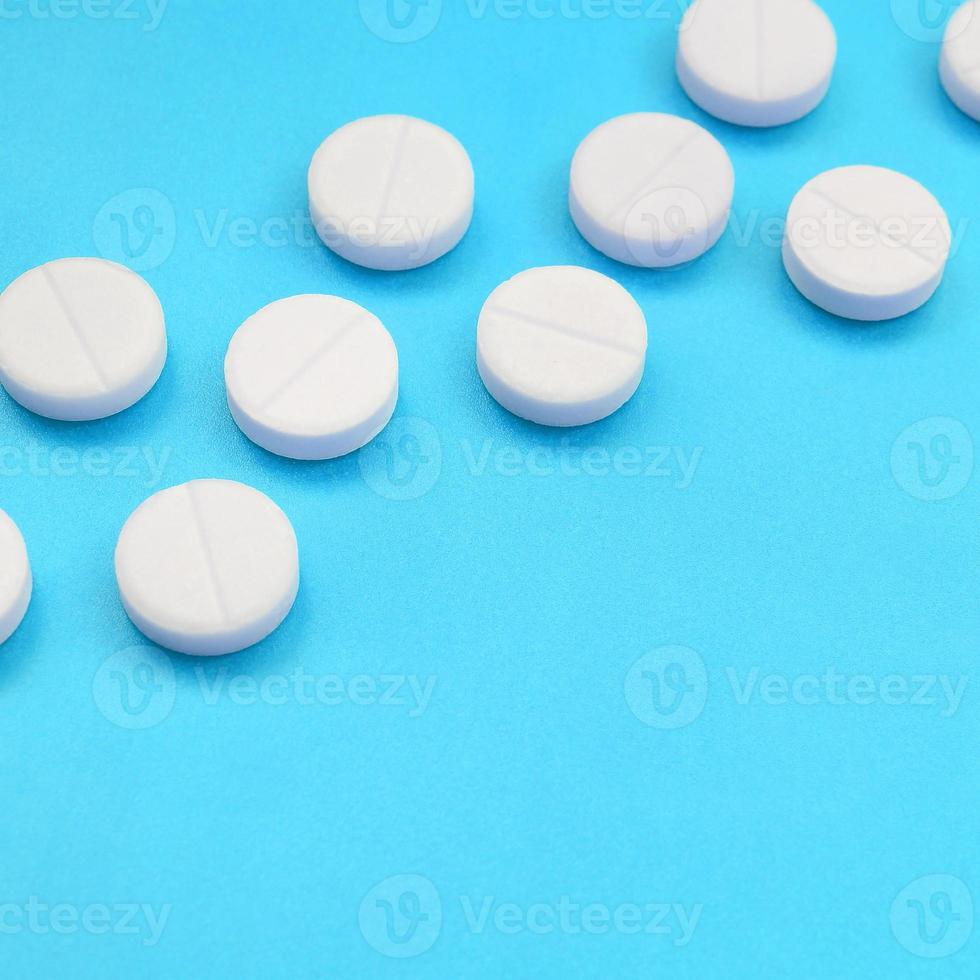 A few white tablets lie on a bright blue background surface. Background image on medical and pharmaceutical topics photo