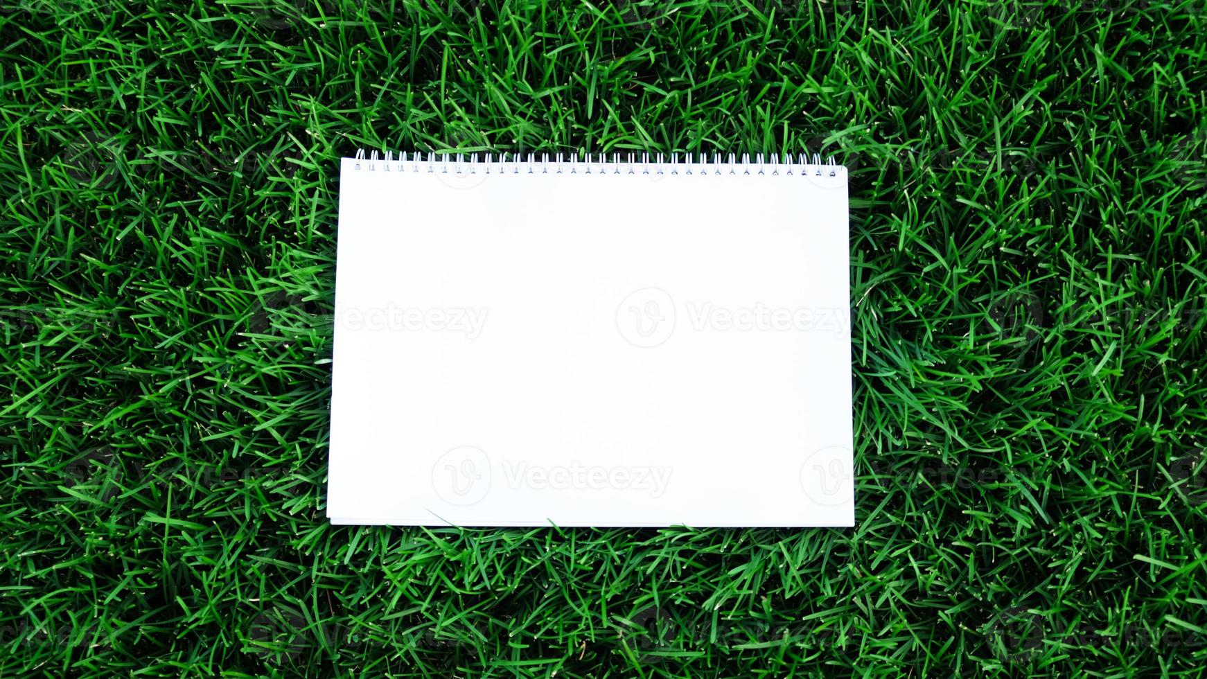 Empty white paper on green grass background. For message flat lay with copy space for text or products presentation. Nature concept, business and lifestyle environment. photo