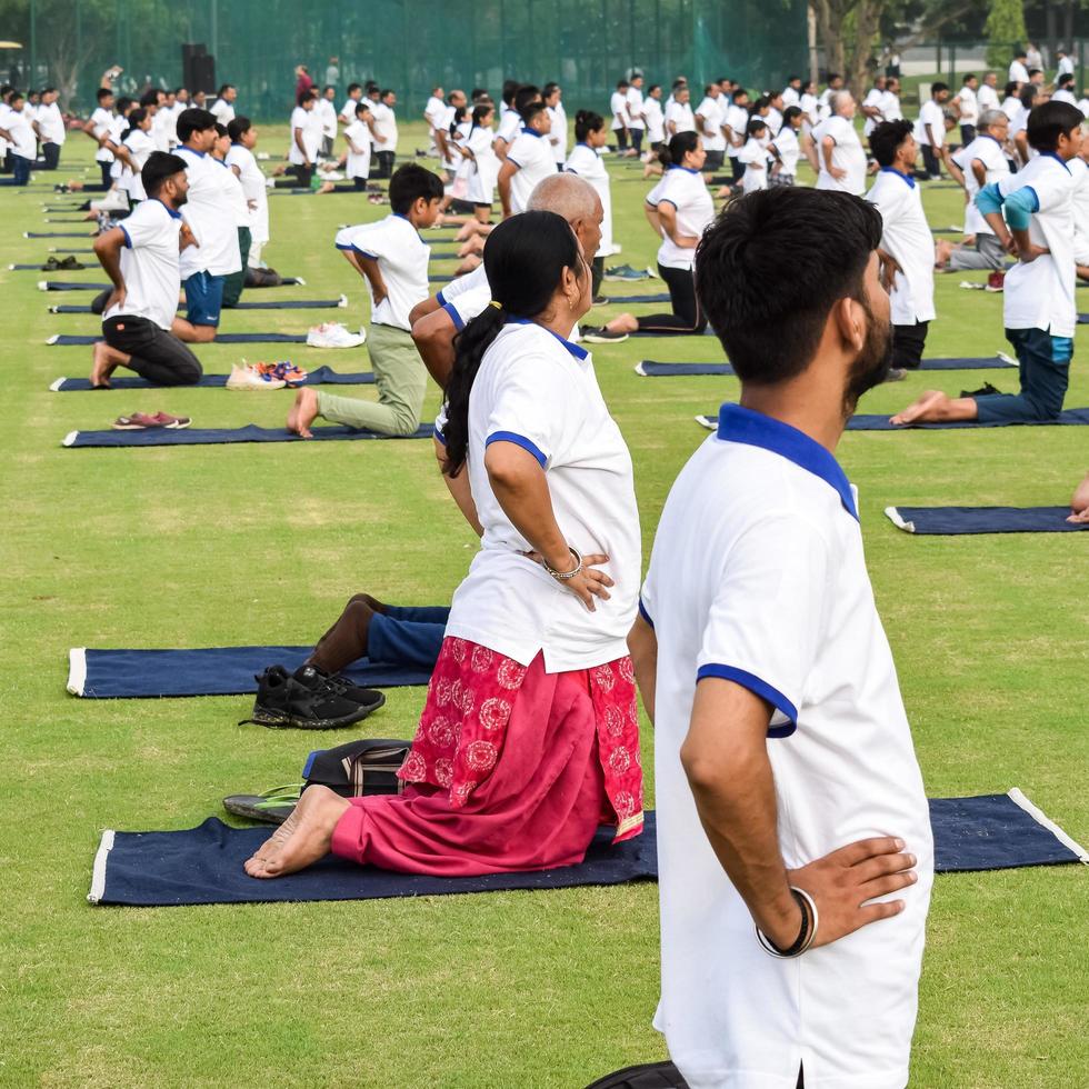 nueva delhi, india, 21 de junio de 2022 - sesión grupal de ejercicios de yoga para personas en el complejo deportivo yamuna en delhi el día internacional del yoga, gran grupo de adultos que asisten a clases de yoga en el estadio de cricket foto