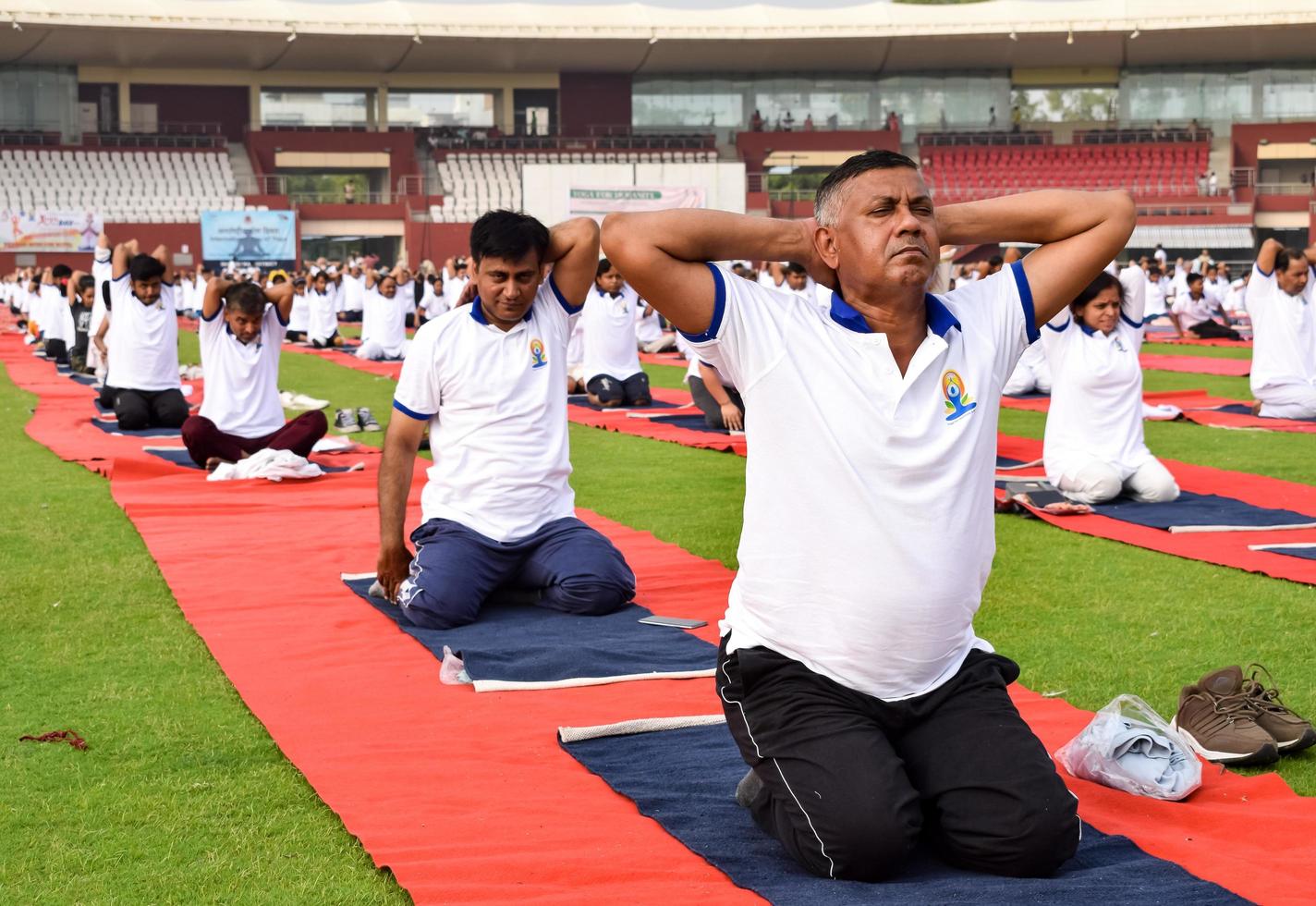 nueva delhi, india, 21 de junio de 2022 - sesión grupal de ejercicios de yoga para personas en el complejo deportivo yamuna en delhi el día internacional del yoga, gran grupo de adultos que asisten a clases de yoga en el estadio de cricket foto