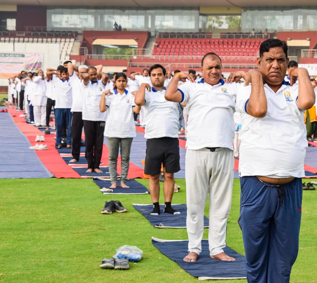 nueva delhi, india, 21 de junio de 2022 - sesión grupal de ejercicios de yoga para personas en el complejo deportivo yamuna en delhi el día internacional del yoga, gran grupo de adultos que asisten a clases de yoga en el estadio de cricket foto