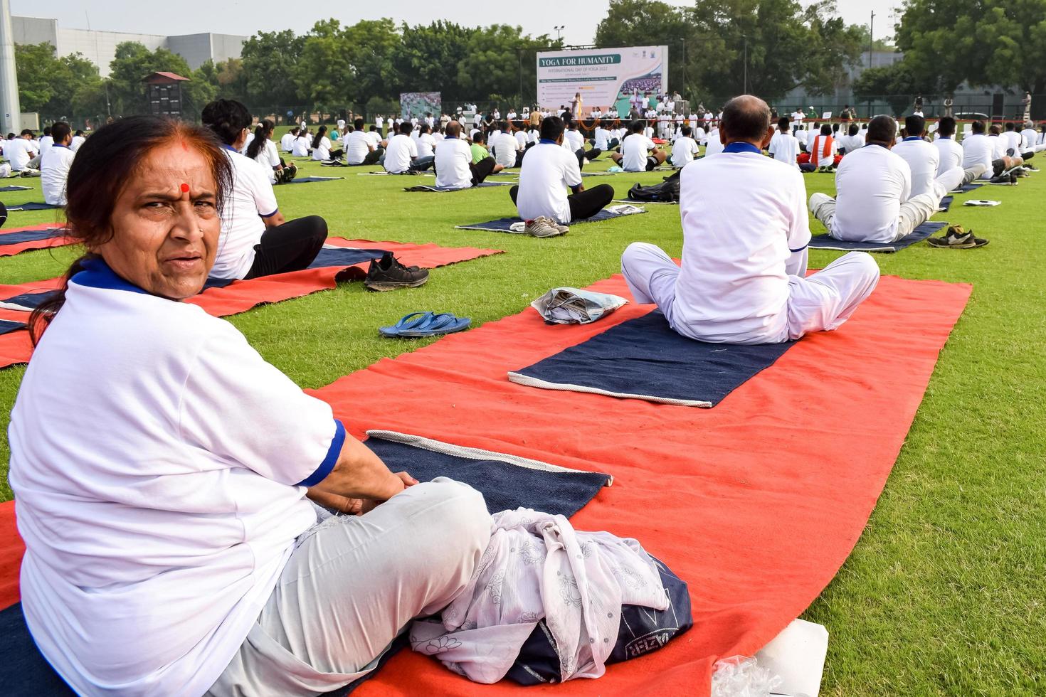 nueva delhi, india, 21 de junio de 2022 - sesión grupal de ejercicios de yoga para personas en el complejo deportivo yamuna en delhi el día internacional del yoga, gran grupo de adultos que asisten a clases de yoga en el estadio de cricket foto