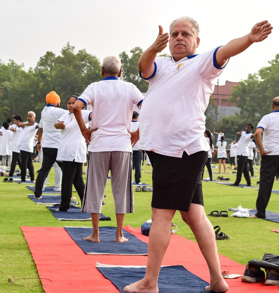 nueva delhi, india, 21 de junio de 2022 - sesión grupal de ejercicios de yoga para personas en el complejo deportivo yamuna en delhi el día internacional del yoga, gran grupo de adultos que asisten a clases de yoga en el estadio de cricket foto
