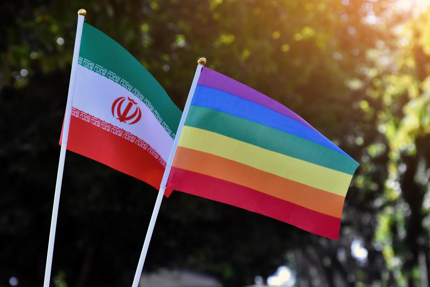 Iran national flag and rainbow flag stand together against bluesky background, concept for lgbt celebration and respecting gender diversity of human in Iran, soft and selective focus. photo