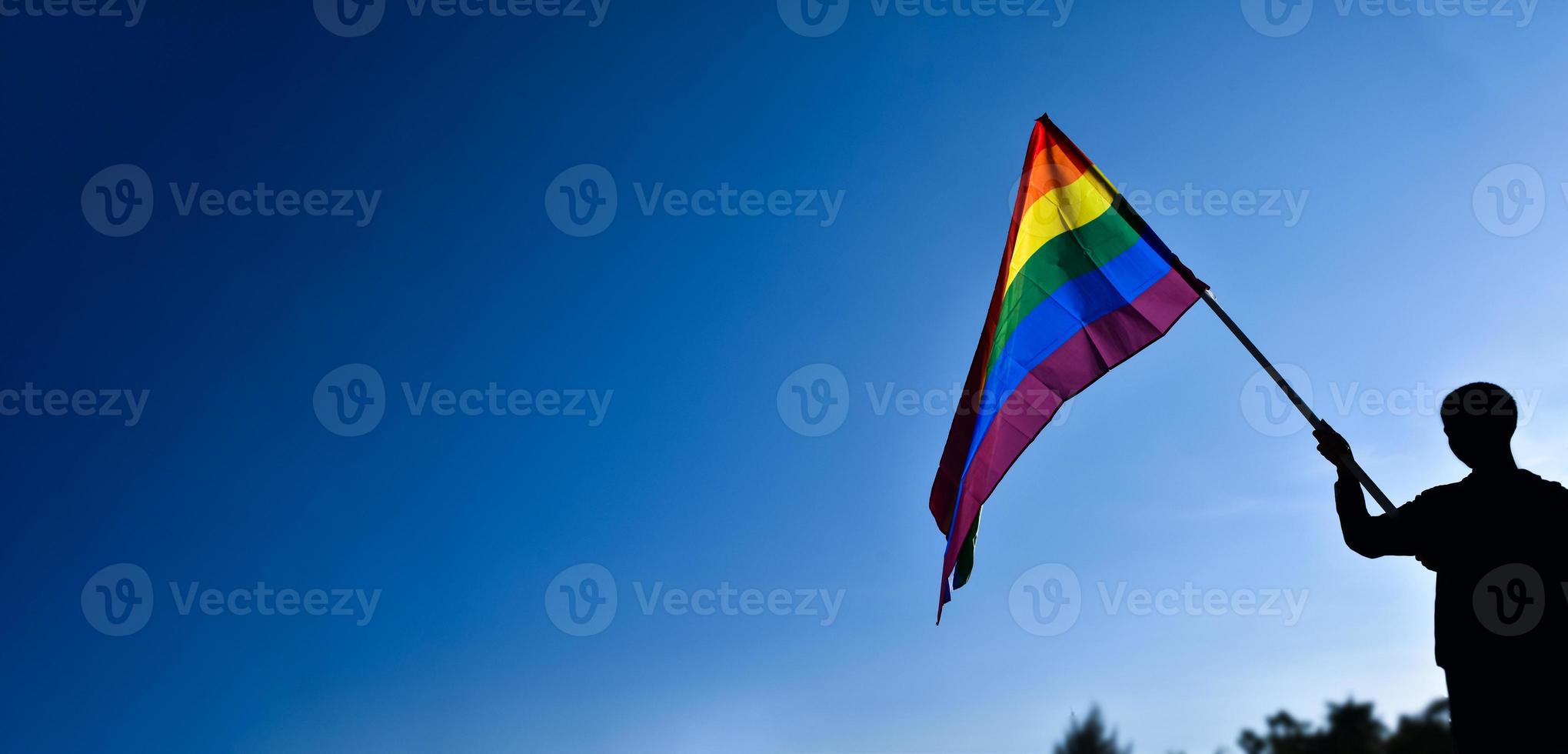 Look up view of rainbow flag, LGBT simbol, against clear bluesky background, soft and  selective focus, concept for LGBT celebration in pride month, June, around the world, copy space. photo