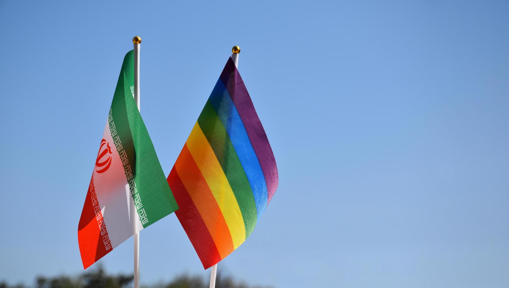Iran national flag and rainbow flag stand together against bluesky background, concept for lgbt celebration and respecting gender diversity of human in Iran, soft and selective focus. photo