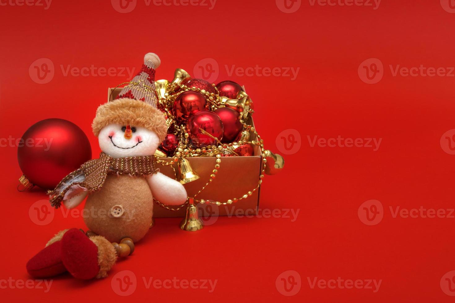 snowman next to Christmas balls and toys on a red background with copy space, Christmas card photo