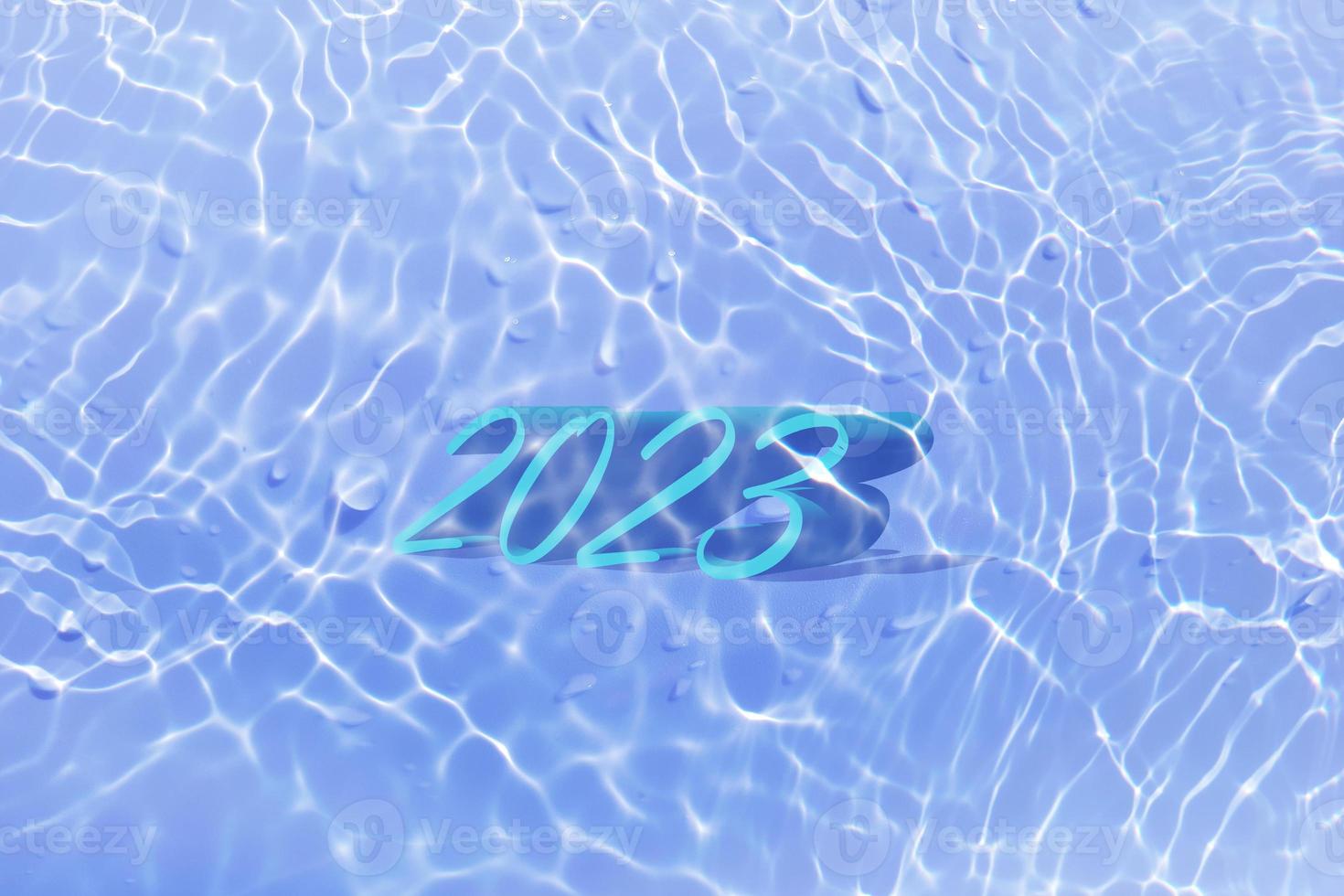 The numbers 2023 lying on water in swimming pool. Defocus blurred transparent blue colored clear calm water surface texture with splashes and bubbles. Trendy abstract nature background. New year 2023. photo