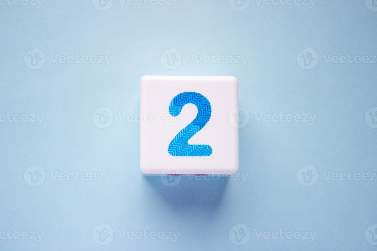 Close-up photo of a white plastic cube with a blue number 2 on a blue background. Object in the center of the photo