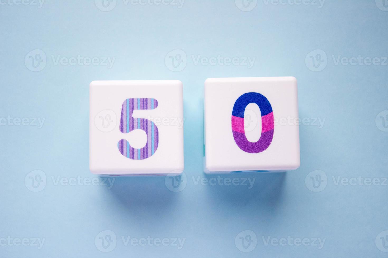 Close-up photo of a white plastic cubes with a colorful number 50 on a blue background. Object in the center of the photo