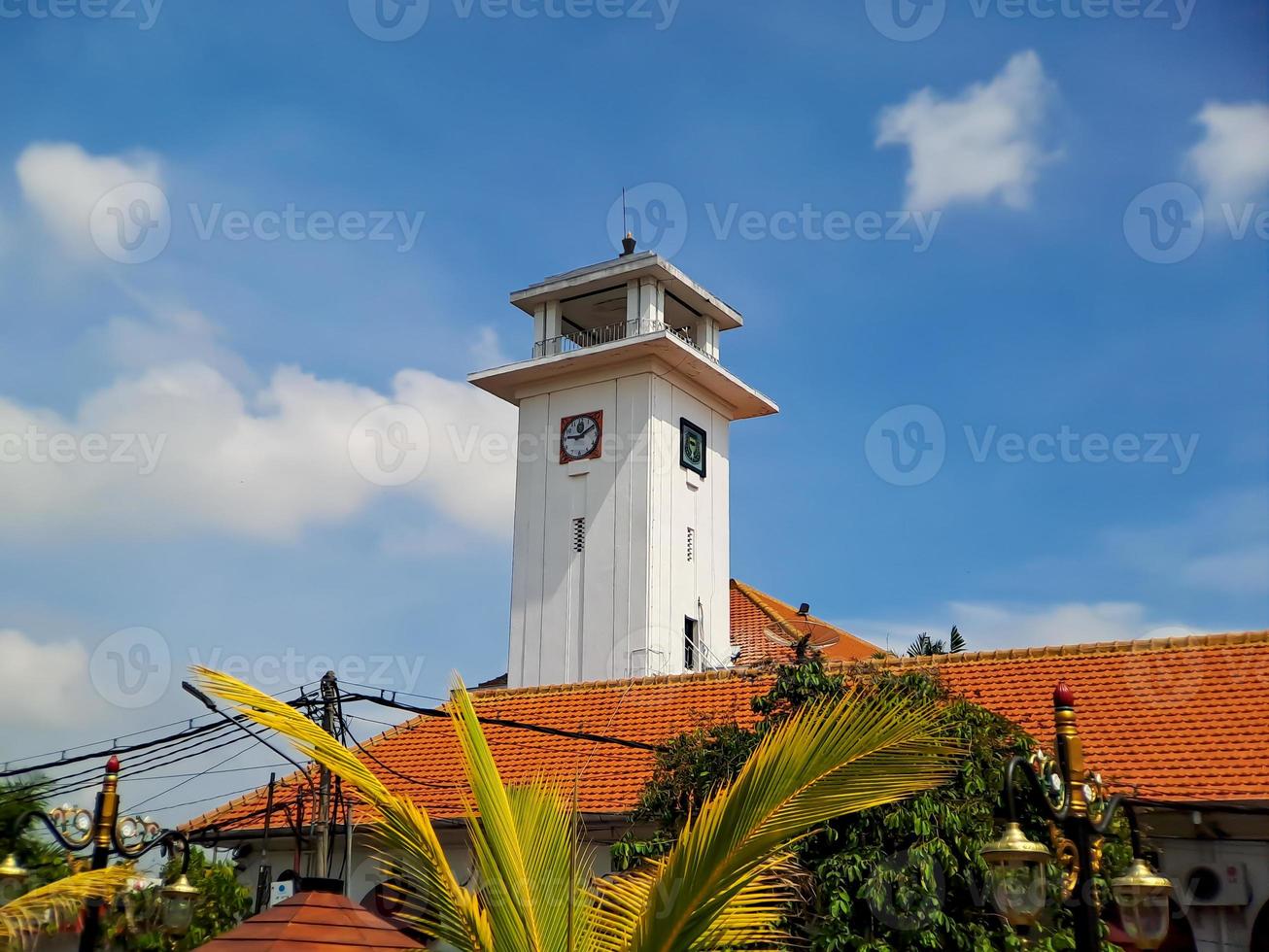Big wall clock in an old white building in Madiun, East Java, Indonesia, with a beautiful bright blue sky. photo