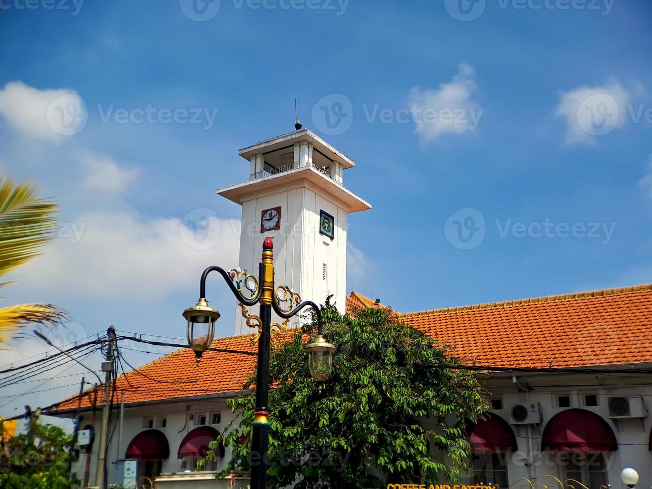 Big wall clock in an old white building in Madiun, East Java, Indonesia, with a beautiful bright blue sky. photo