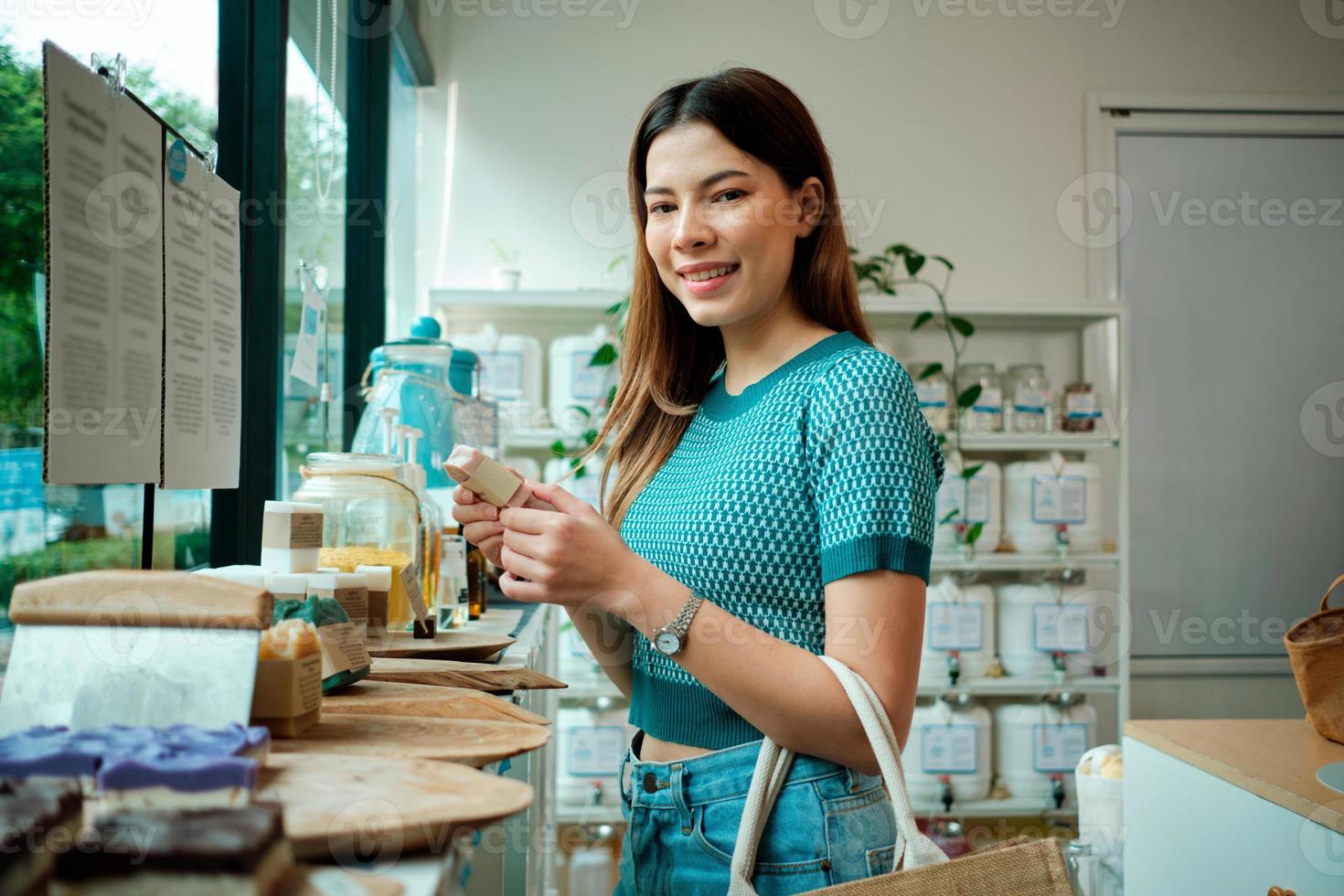 A young Caucasian woman chooses and shops for reusable and recycled appliance products, soap in refill store, zero-waste grocery, and plastic-free, environment-friendly, sustainable lifestyle. photo
