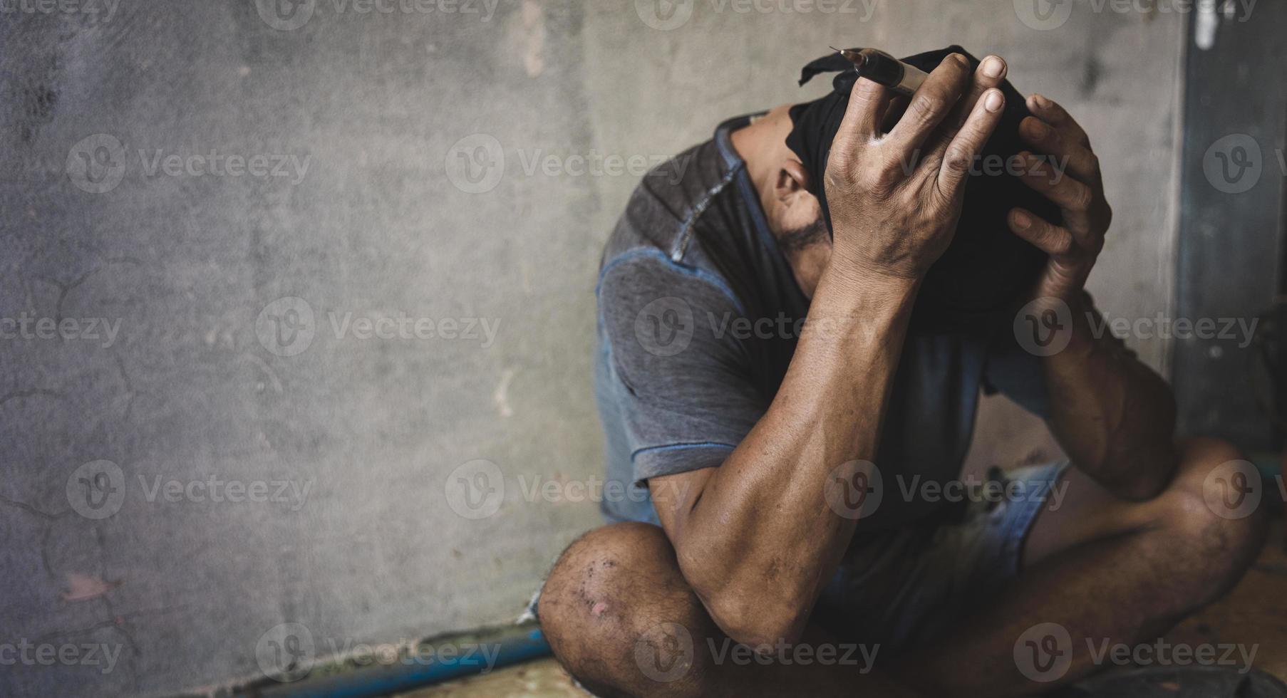 concepto de adicción a las drogas y síntomas de abstinencia. hombre deprimido y sin esperanza sentado solo después de usar drogas y beber alcohol en una casa abandonada. personas sin hogar, día internacional contra el uso indebido de drogas. foto