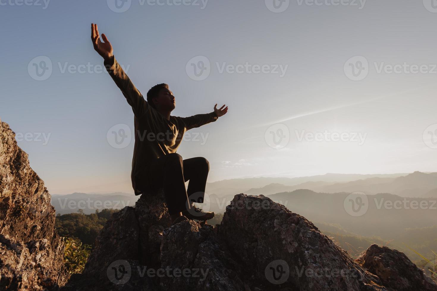 silhouette of man rise hand up praying  on top of mountain and sunset sky abstract background. Freedom and travel adventure concept. photo