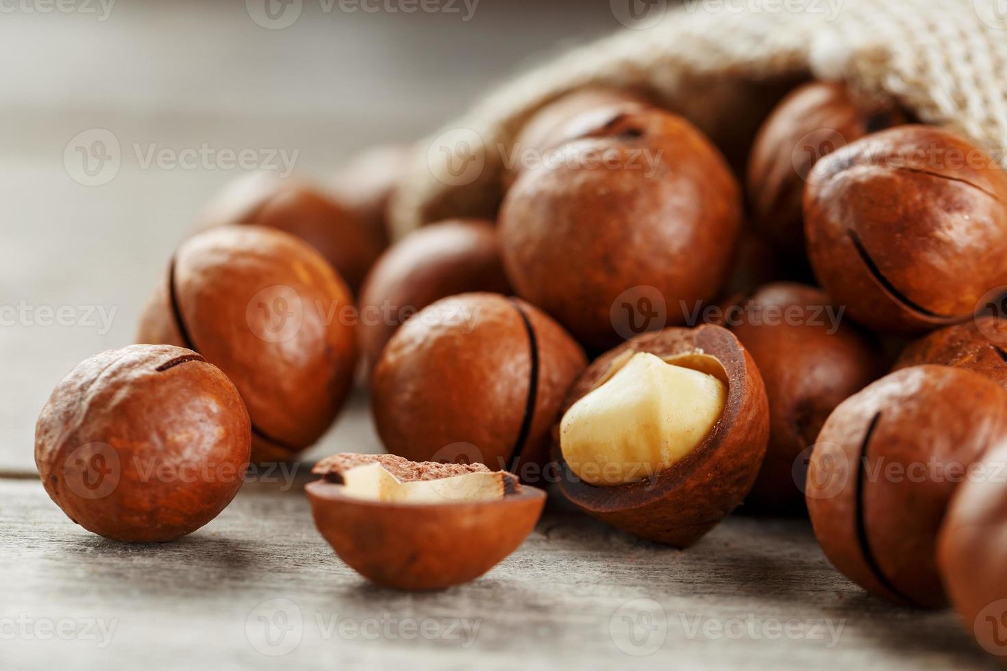 nueces de macadamia derramadas de la bolsa sobre un fondo de madera con una nuez pelada foto