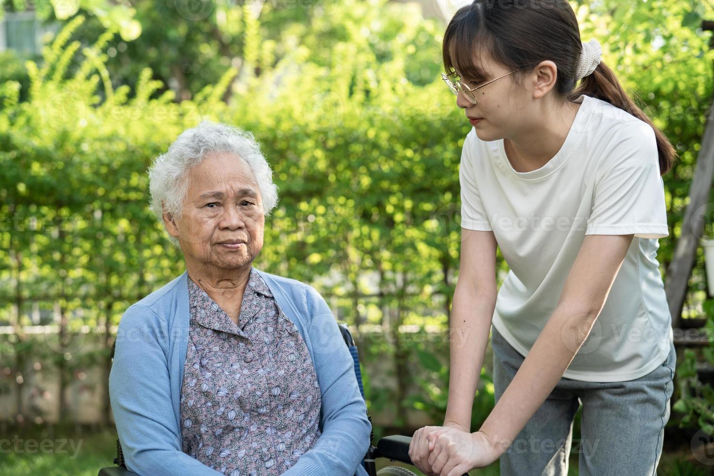 cuidador ayuda y cuida a una anciana asiática o anciana paciente sentada en silla de ruedas en el parque, concepto médico fuerte y saludable. foto