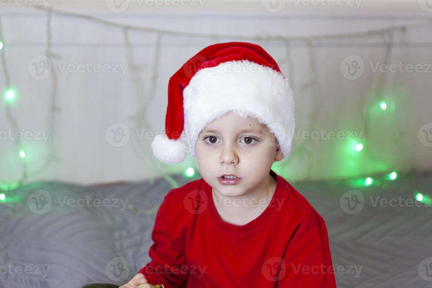 Portrait of a cute boy in a Santa Claus hat. Funny smiling child. Gifts, toys, joy, celebration. photo